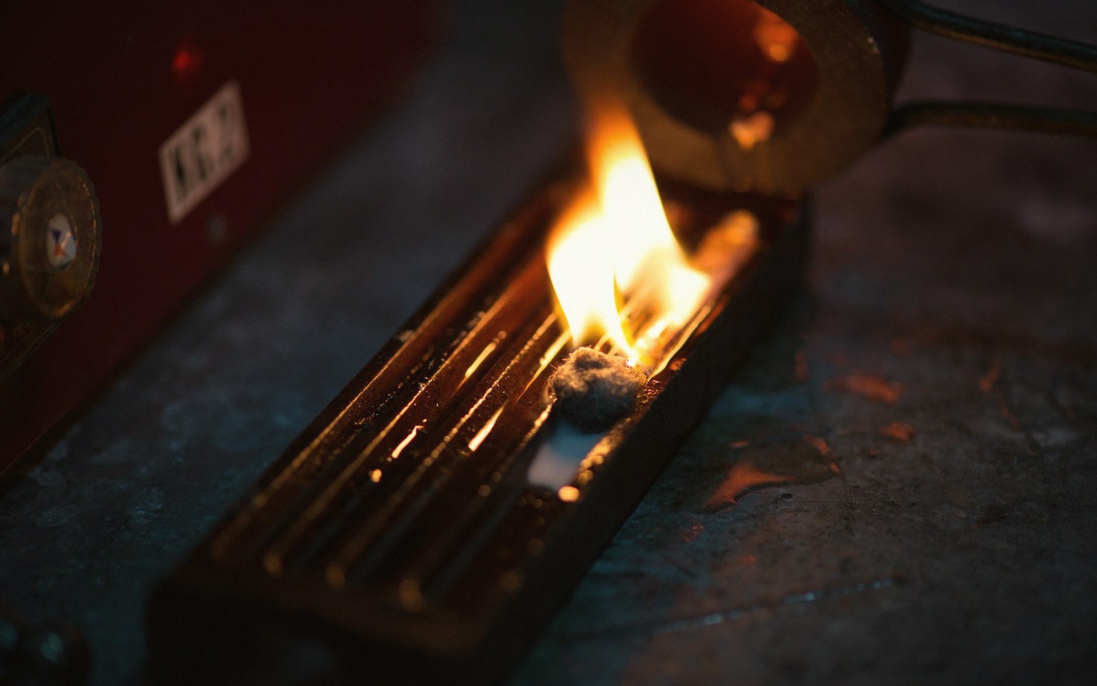 A candle mid-burn-test with a small steel ruler resting against the vessel to indicate melt pool depth, notebook visible at the edge of frame