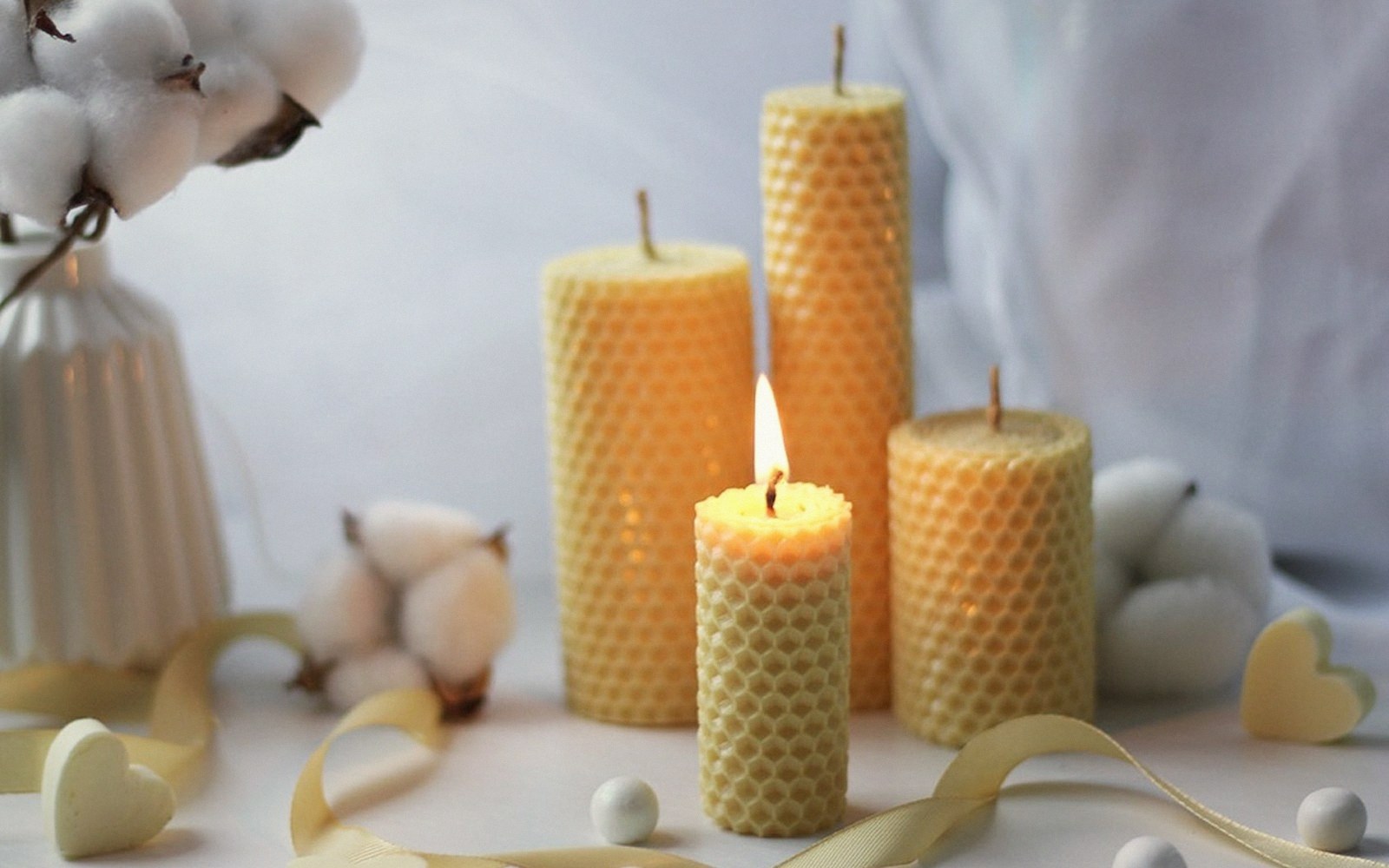 Rolled beeswax candles with honeycomb texture arranged beside cotton stems and ribbon