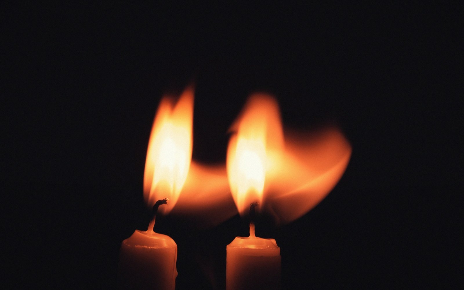 Two lit candles with flickering flames flaring sideways against a dark background