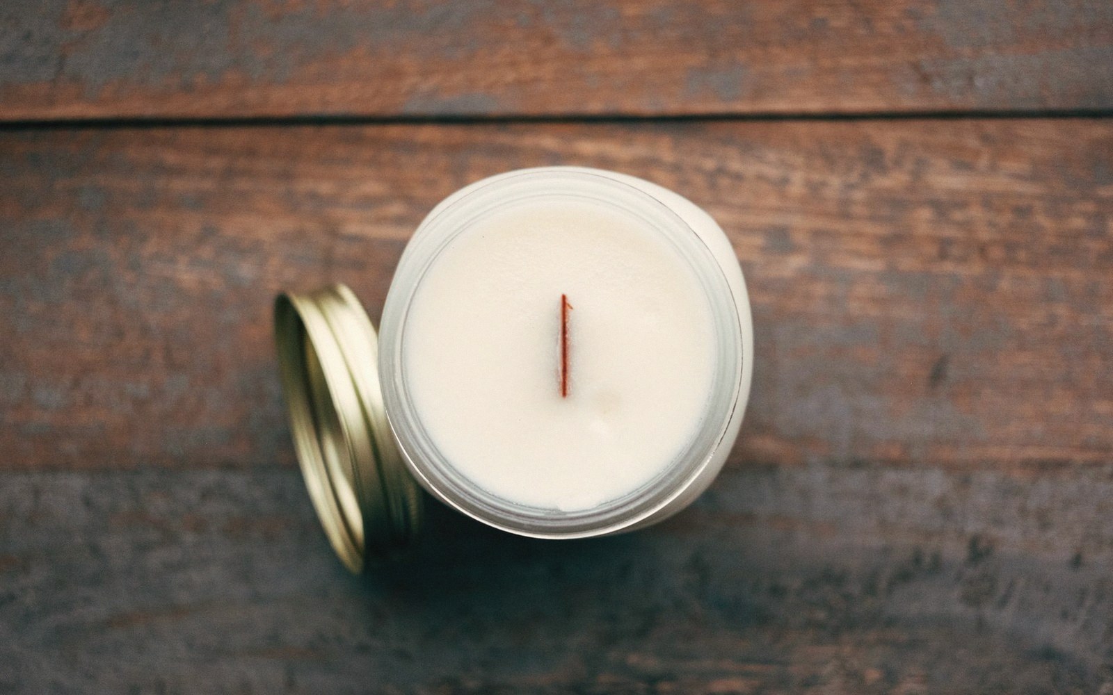 Overhead view of an unlit candle in a glass jar with lid beside it