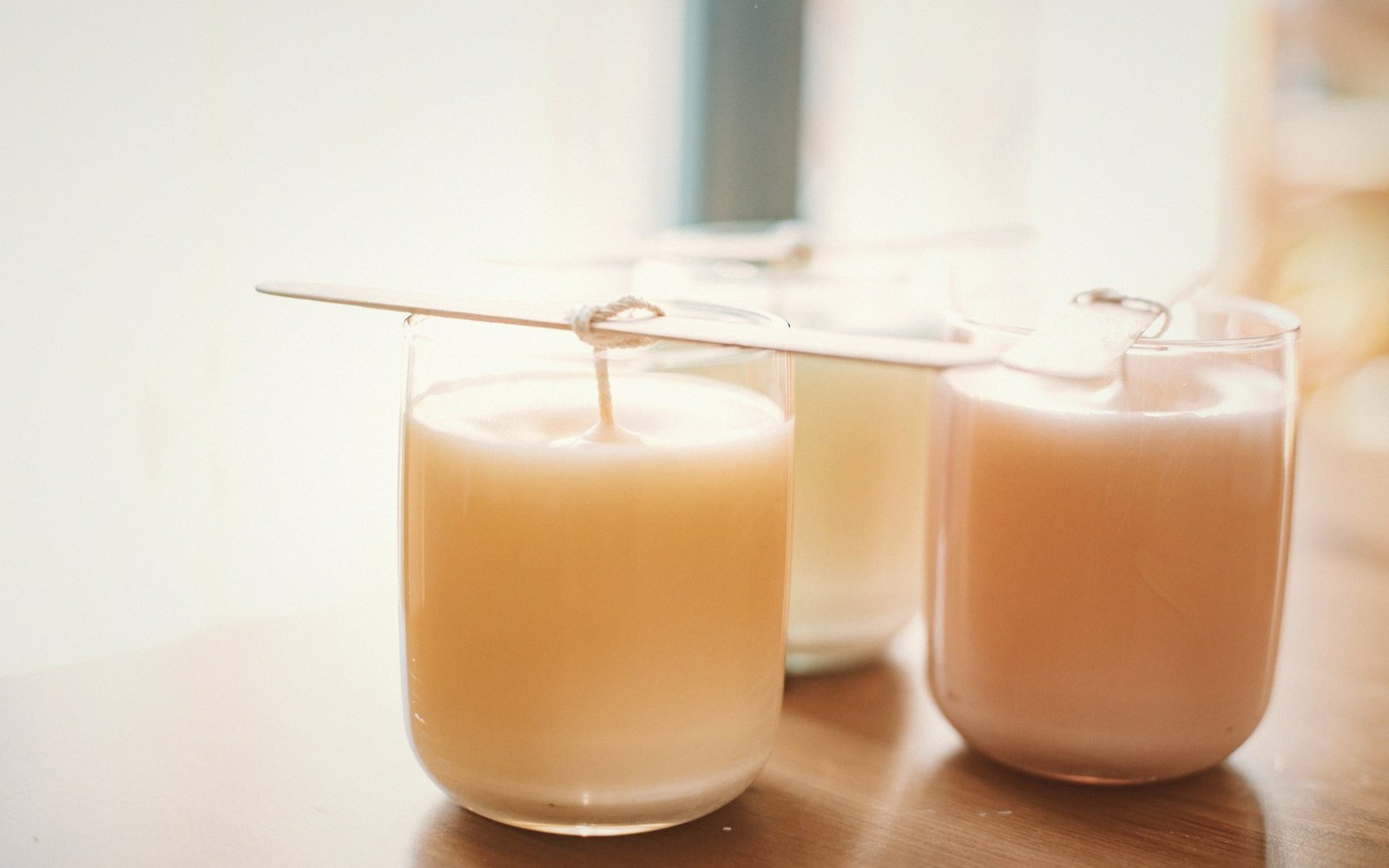 Three glass candles with wicks tied to sticks, wax still setting in different colors