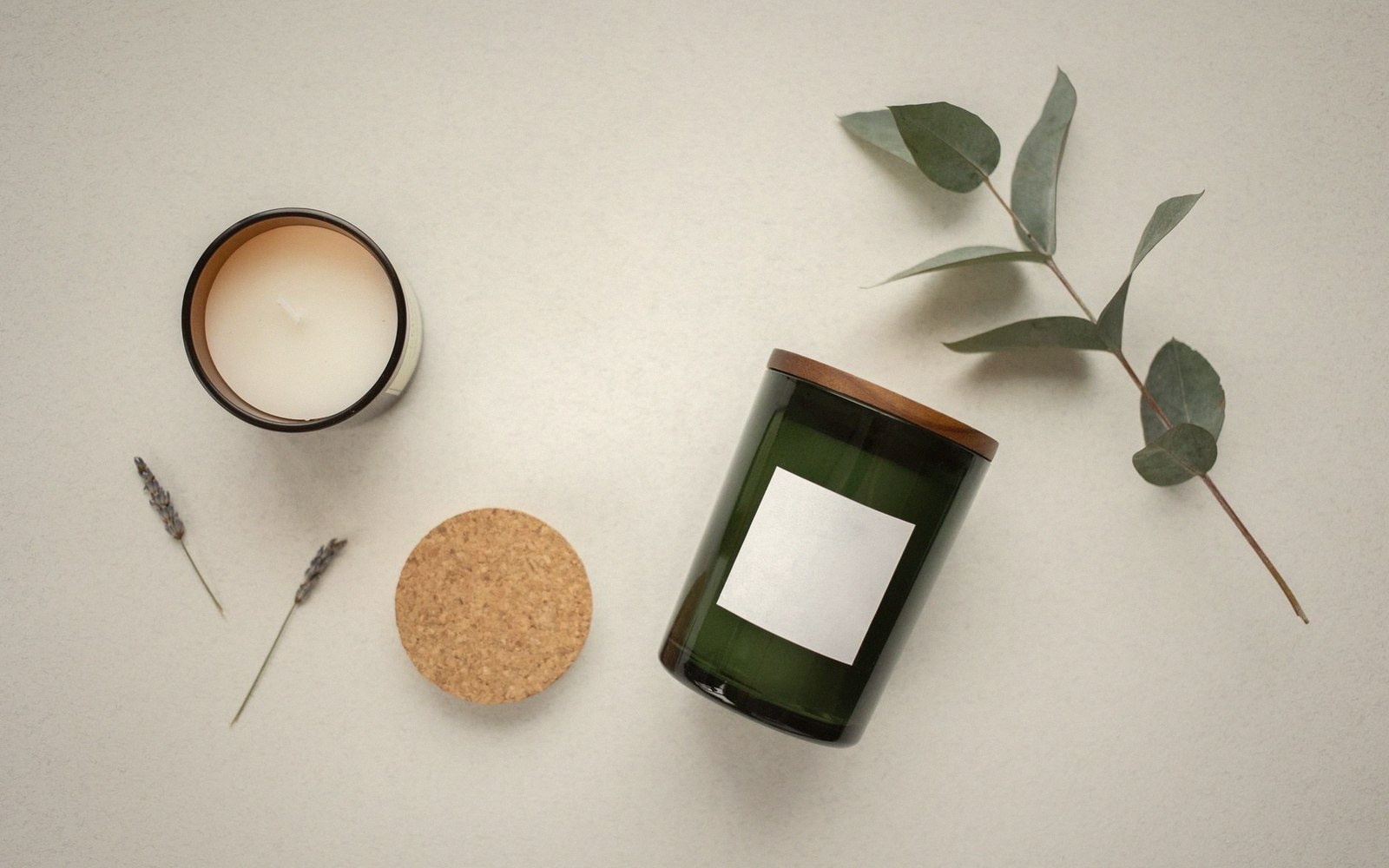 Two candles with a cork lid, dried lavender sprigs and a eucalyptus branch on beige