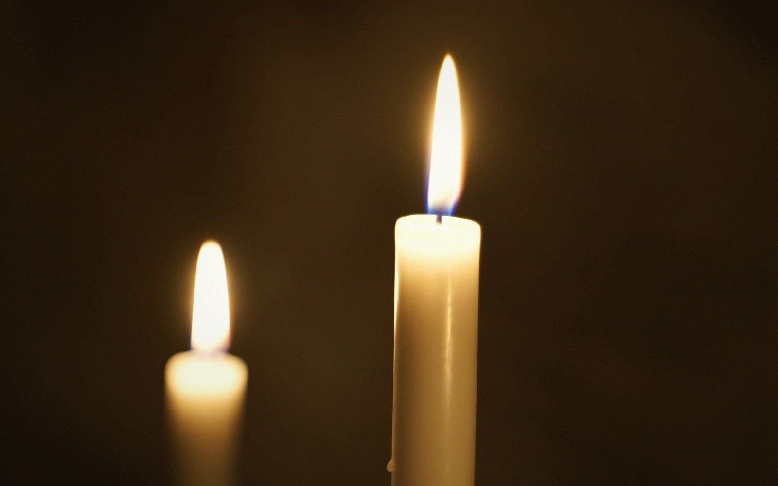 Two lit white candles glowing against a dark background, one closer and taller