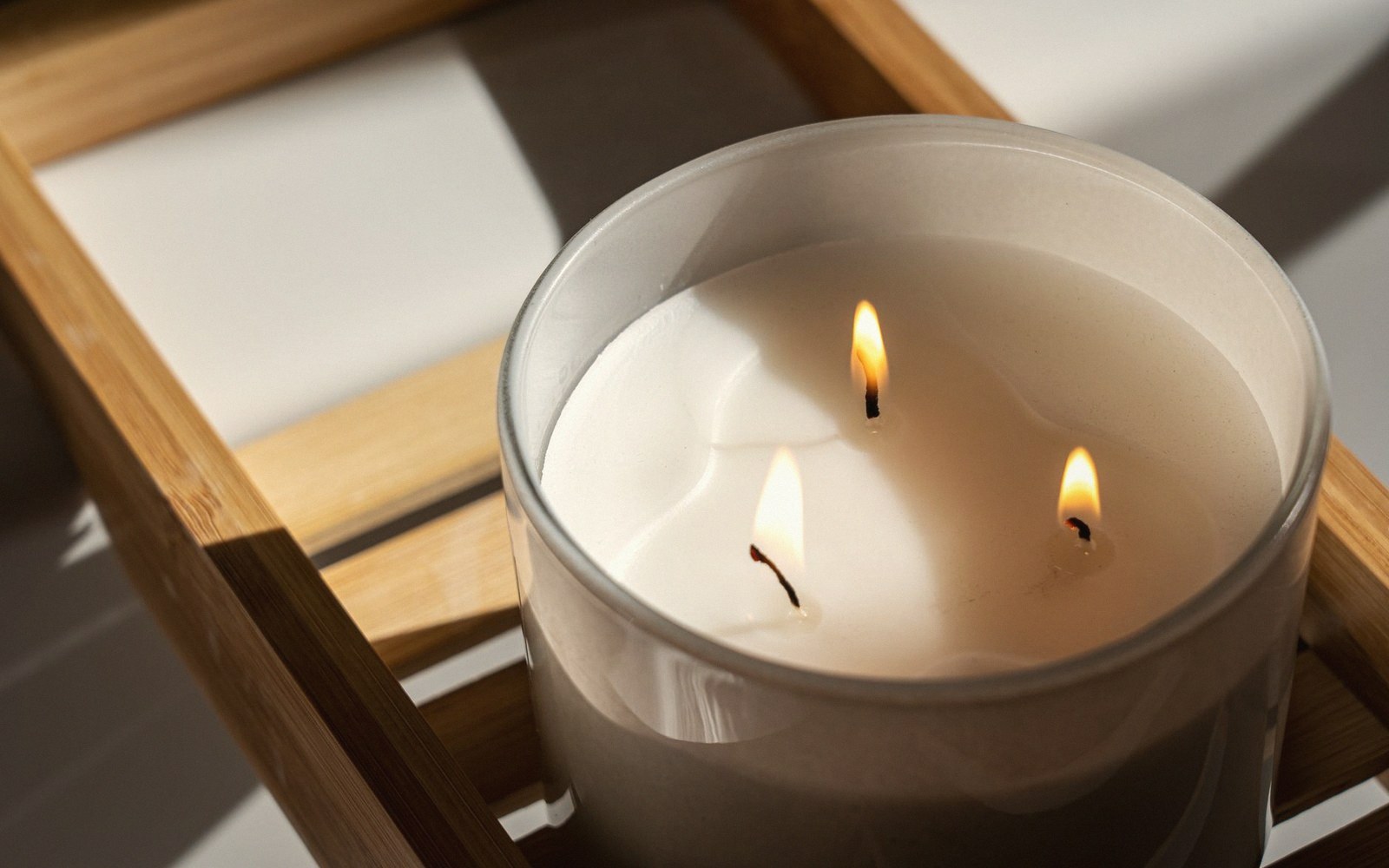 A three-wick candle burning in a glass jar set on a wooden tray