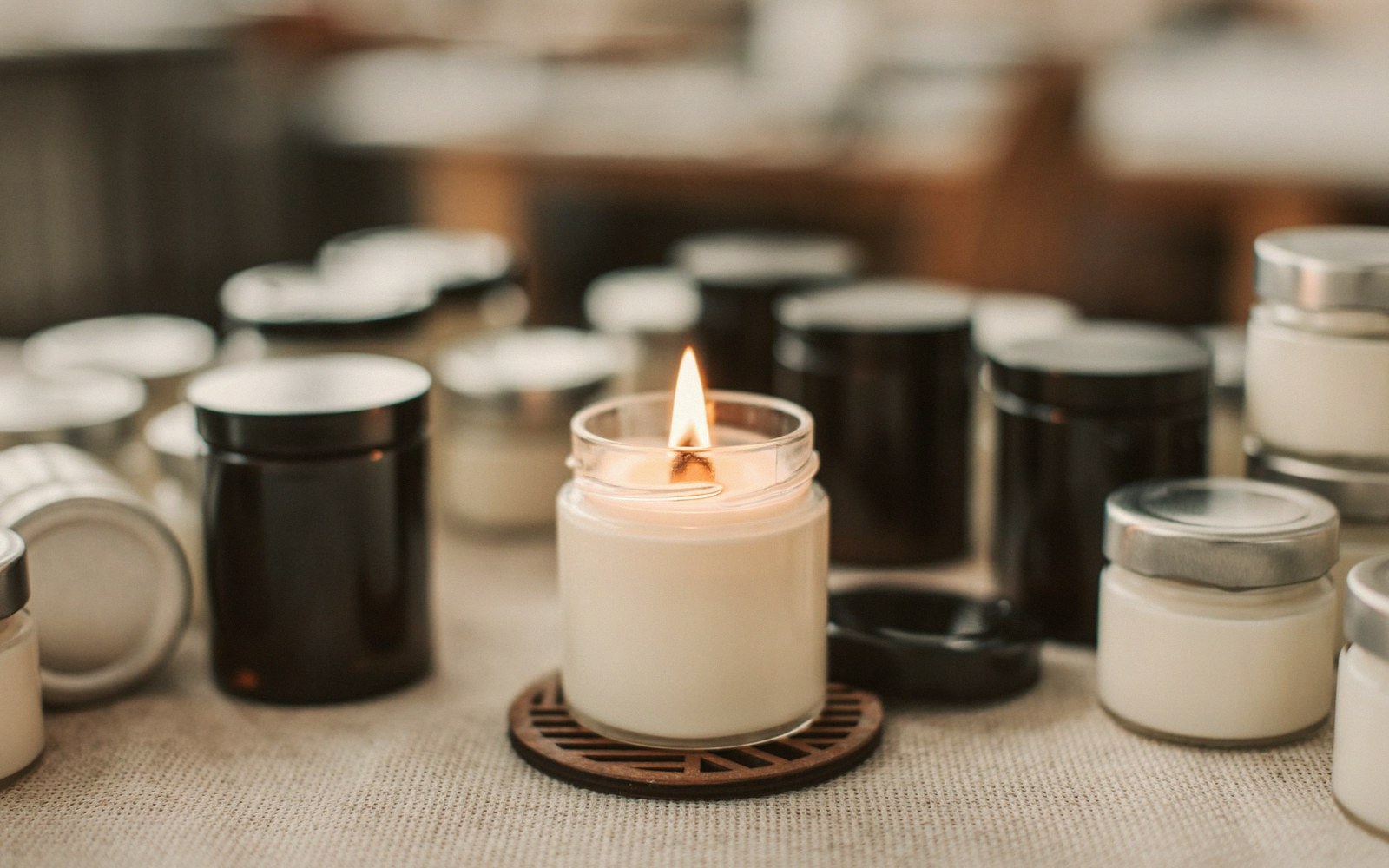 A lit candle in a glass jar surrounded by lidded candle jars on a table