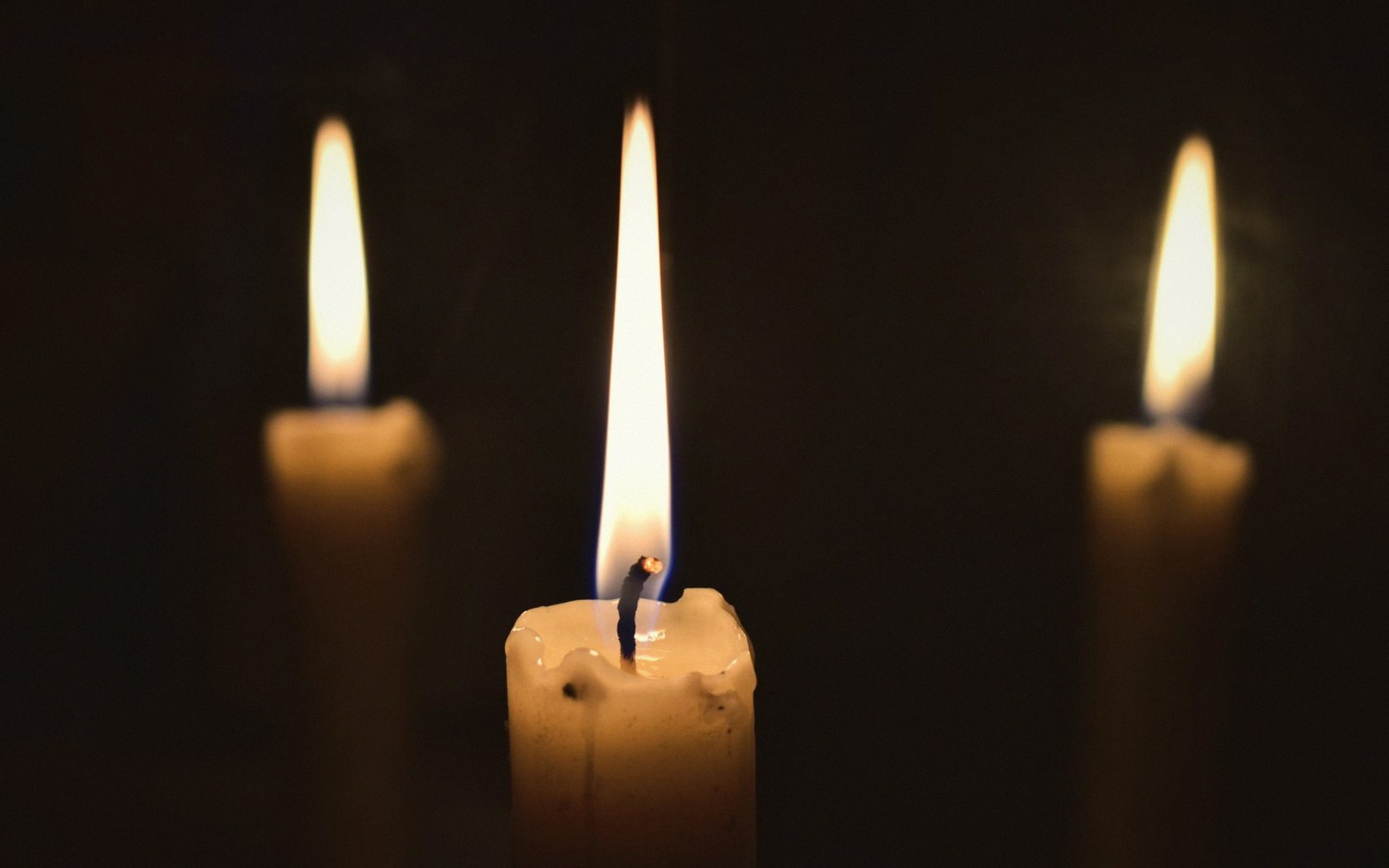 Three lit candles glow against a dark background, the center flame in sharp focus
